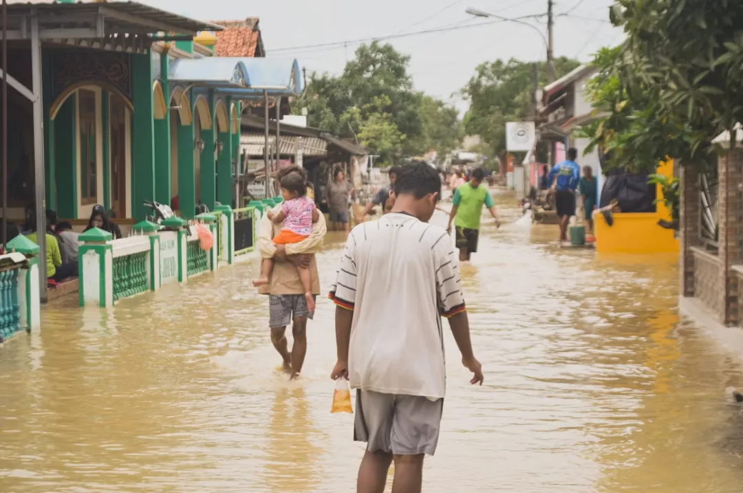 A flooded street, residents wading through knee-deep water